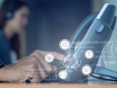 Closeup of a hand interacting with a telephone unit with VOIP icons on the foreground and a call center agent in the background.