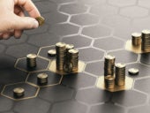 Human hand stacking generic coins over a black background with hexagonal golden shapes.