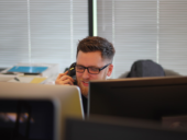 A man with glasses sitting at his desk talking to someone on the phone.